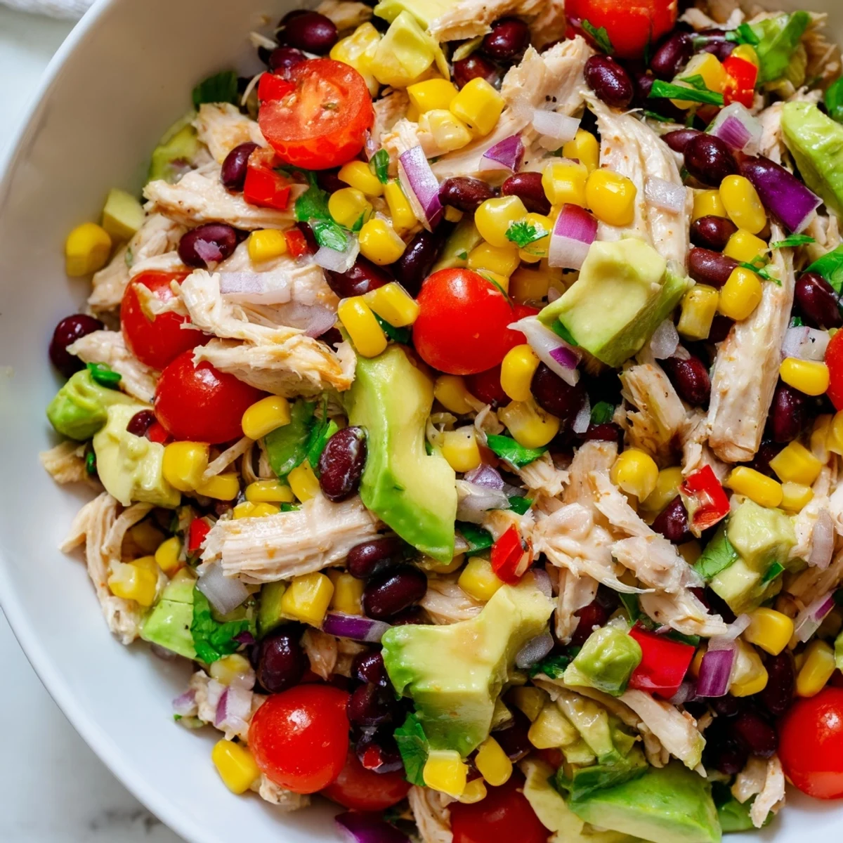 Vibrant bowl of Southwestern Bean Salad with shredded chicken, zesty lime dressing, and crunchy vegetables.