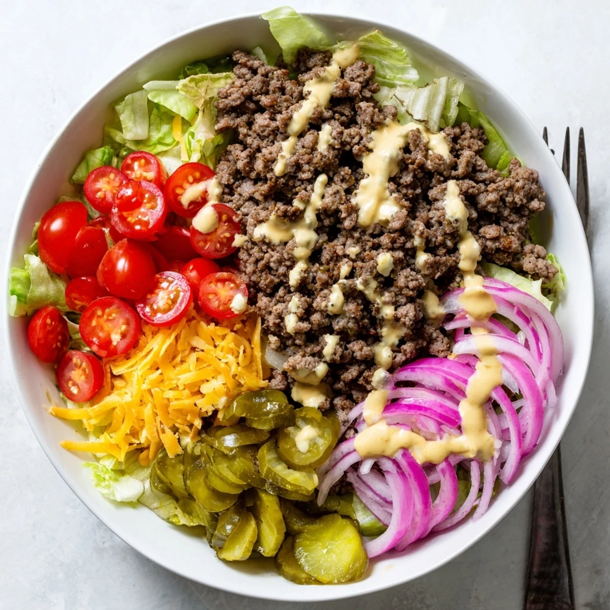 A finished bowl of Easy Big Mac in a Bowl filled with seasoned ground beef, fresh lettuce, tomatoes, onions, pickles, and melted cheddar.