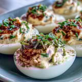 Classic deviled eggs with paprika and chives, creamy yolk filling in halved whites, garnished with smoky spice and fresh herbs.