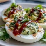 Creamy avocado deviled eggs topped with a spicy Sriracha drizzle, perfect for healthy party appetizers.  