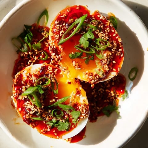 A close-up of Chili Oil Eggs: perfectly poached eggs coated with glistening, flavorful chili oil sauce.