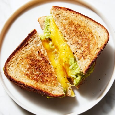 A close-up of a perfectly toasted Avocado Toast Grilled Cheese, oozing melted cheese between golden bread.