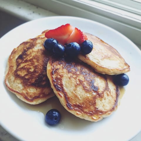 Banana Pancakes rest on a white plate with a cup of coffee, showcasing their fluffy texture and sweet aroma.