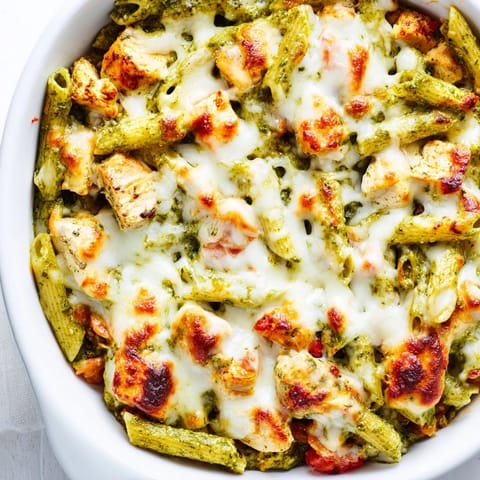 Steam rises from the cheesy Pesto Chicken Pasta Bake, featuring tender chicken pieces and vibrant green pesto swirls.
