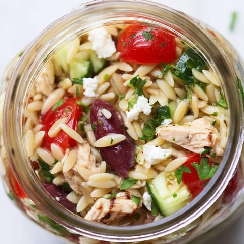 A single jar of Greek Pasta Chicken Salad with orzo, chicken, olives, and parsley, ready to grab and go.
