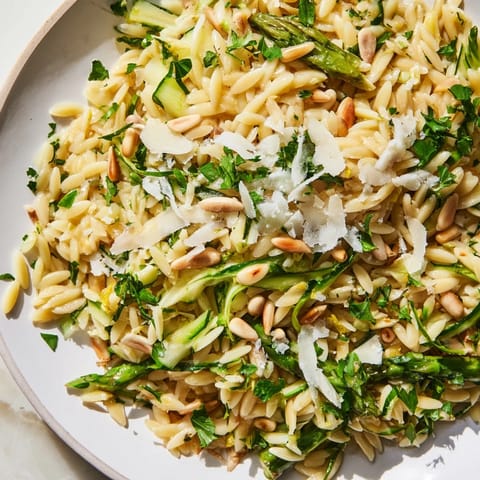 This fresh Asparagus Lemon Orzo Salad is served in a white bowl, garnished with parsley, perfect for spring gatherings.