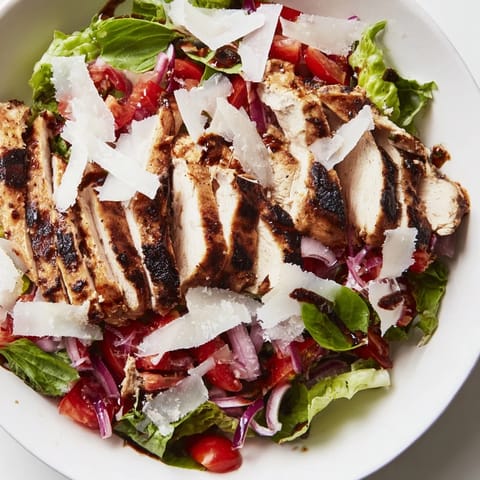 A fresh Bruschetta Chicken Salad features tender grilled chicken, a zesty tomato topping, and crisp greens on a white plate.