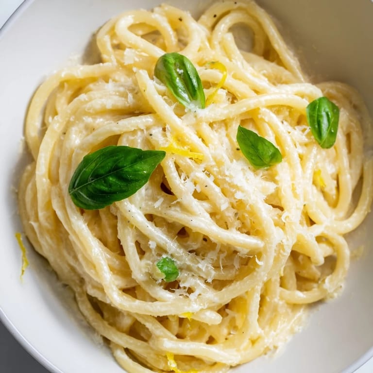 A close-up of Lemon Ricotta Pasta reveals creamy sauce clinging to spaghetti, with a drizzle of olive oil and grated Parmesan.