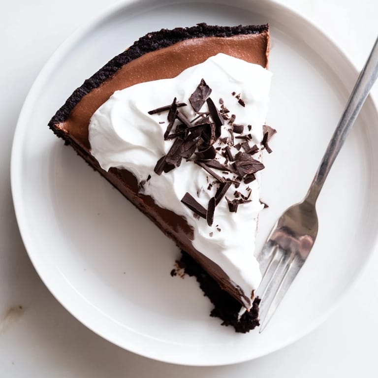 Smooth chocolate cheesecake filling on a cocoa graham crust, garnished with dark chocolate shavings and a drizzle of honey.