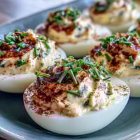 Classic deviled eggs with paprika and chives, creamy yolk filling in halved whites, garnished with smoky spice and fresh herbs.
